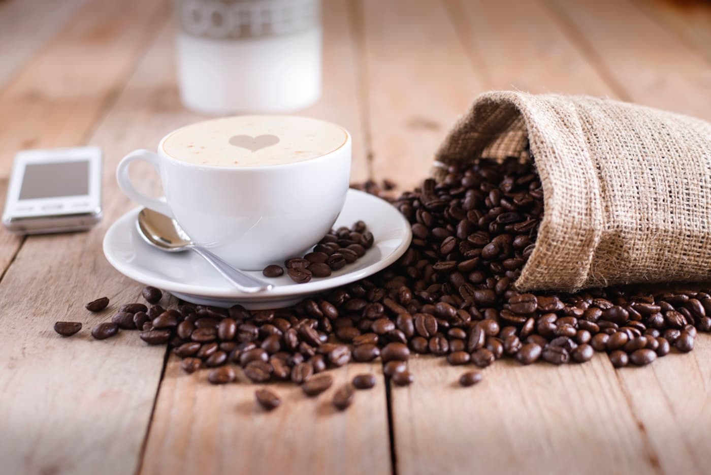 A bag of whole coffee beans beside a fresh cappuccino